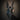 Black goat mask with large horns held against a dark background the blackened teeth